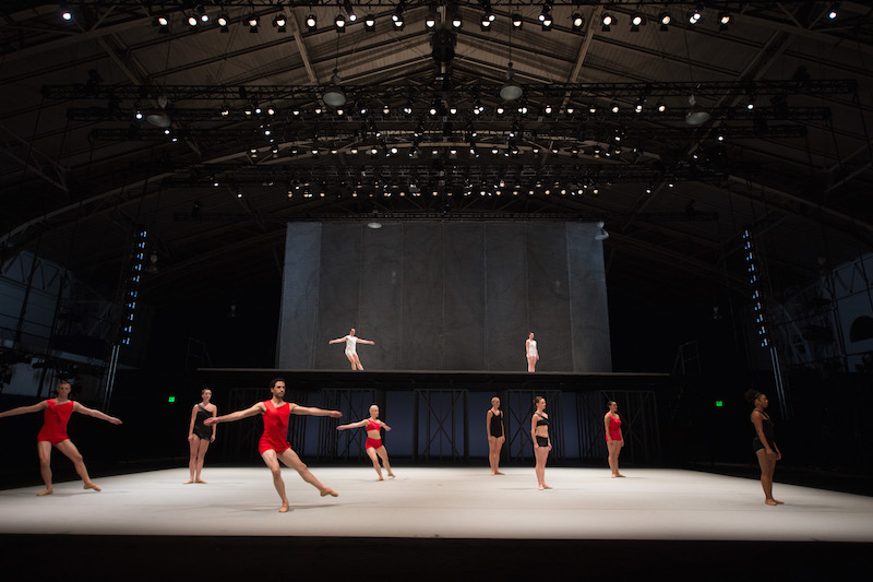 Dancers in black, white and red unitards perform on the first and above stages.